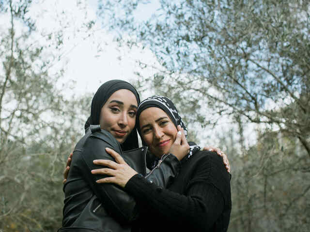 Nour und ihre Mutter Nidal Al-Hajjar umarmen sich und schauen in die Kamera.